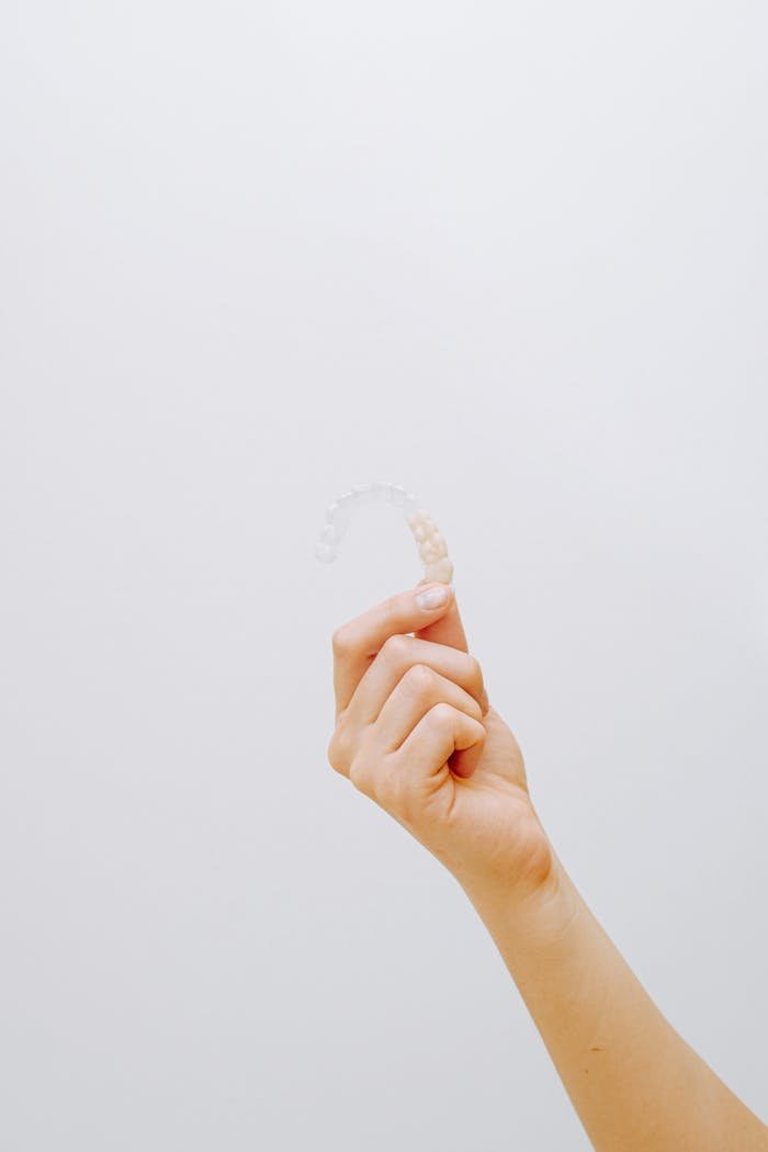 Close-up of a hand holding a clear dental aligner against a white background, emphasizing orthodontic care.